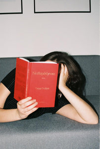 Mergina gulinti ant sofos skaito rašytojos Gabijos Grušaitės knygą „Neišspildymas“